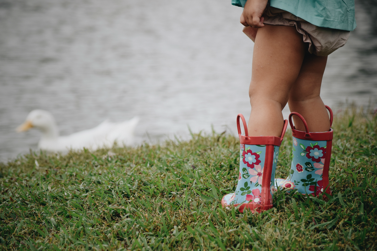 Teal floral rain boots with red trim on a child’s lower legs