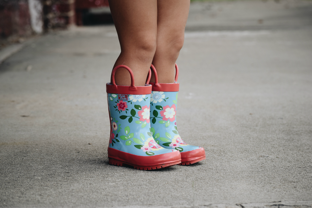 Close view of teal floral rain boots with red handles and rubber tread sole