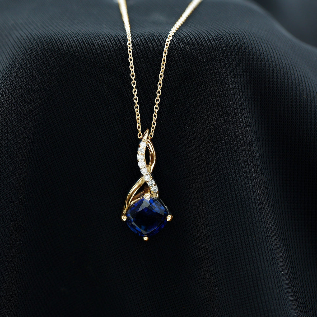 Gold infinity pendant necklace featuring a dark blue cushion sapphire and diamond details