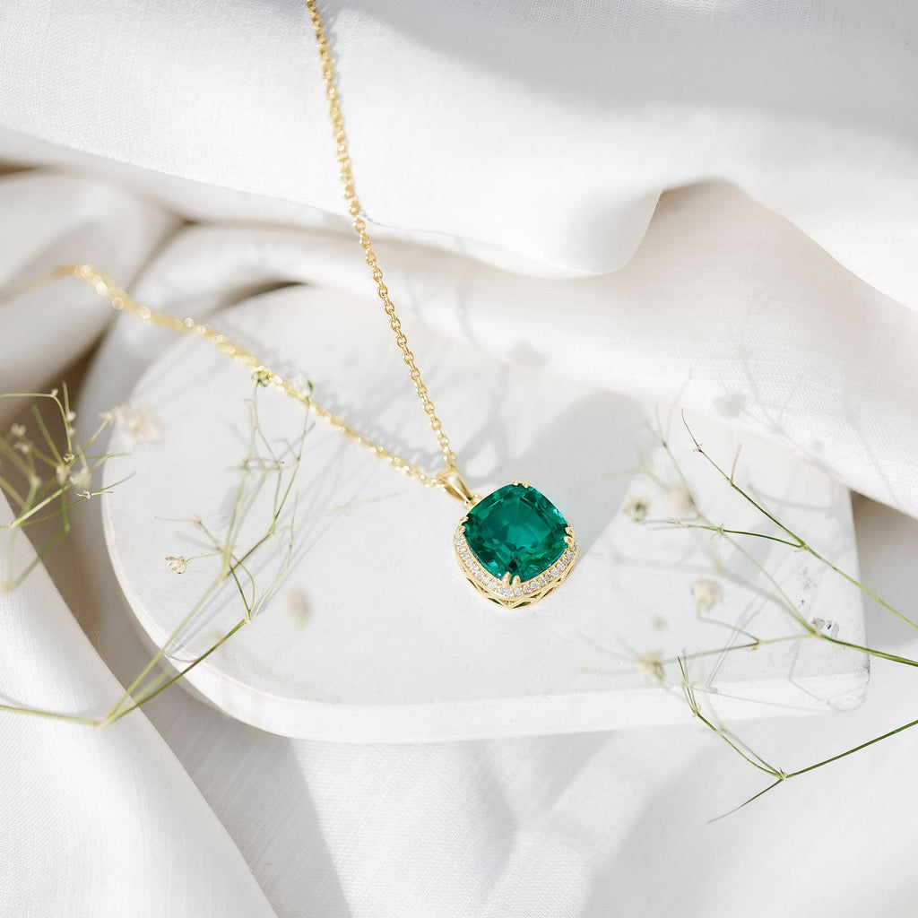 Gold-tone cushion emerald pendant necklace resting on white fabric