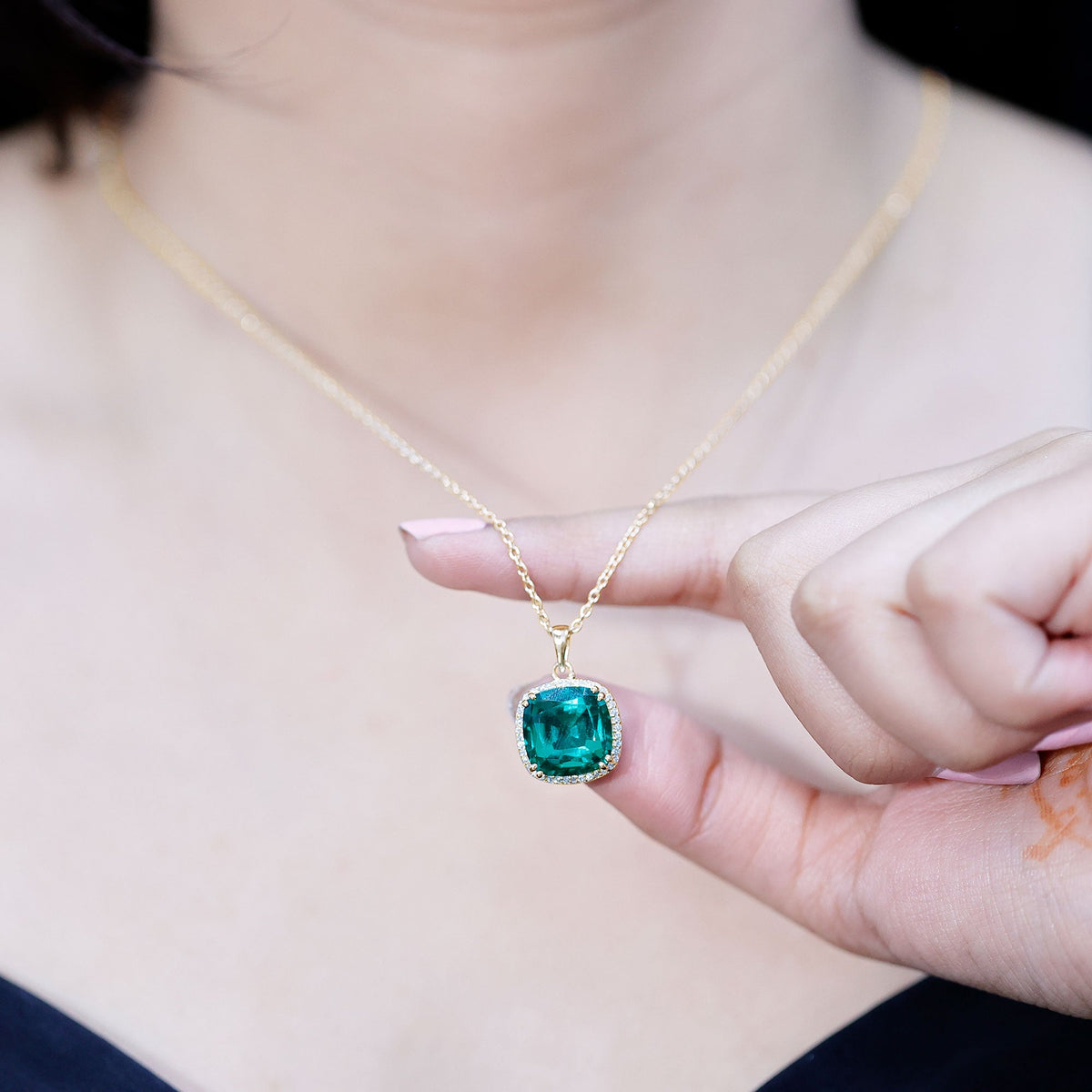 Gold-tone necklace with cushion emerald pendant held in hand