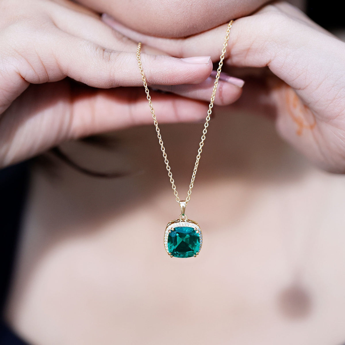 Gold-tone cushion emerald pendant necklace held close-up