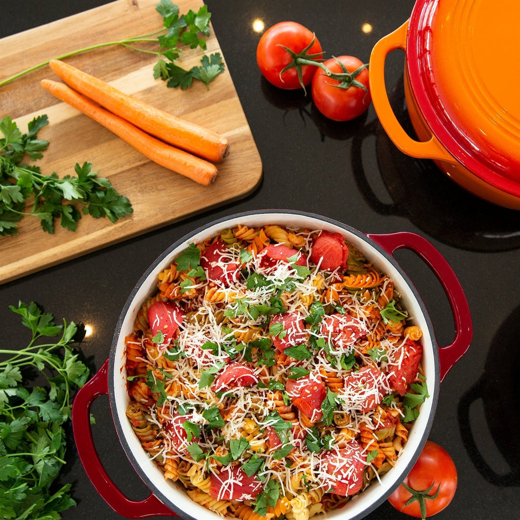 Red Dutch oven filled with spaghetti, tomatoes, and herbs; side handles visible