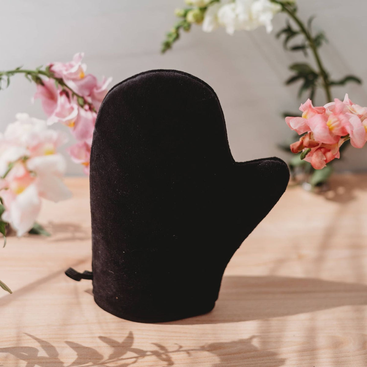 Black self-tanner mitt accessory with drawstring cuff and curved shape