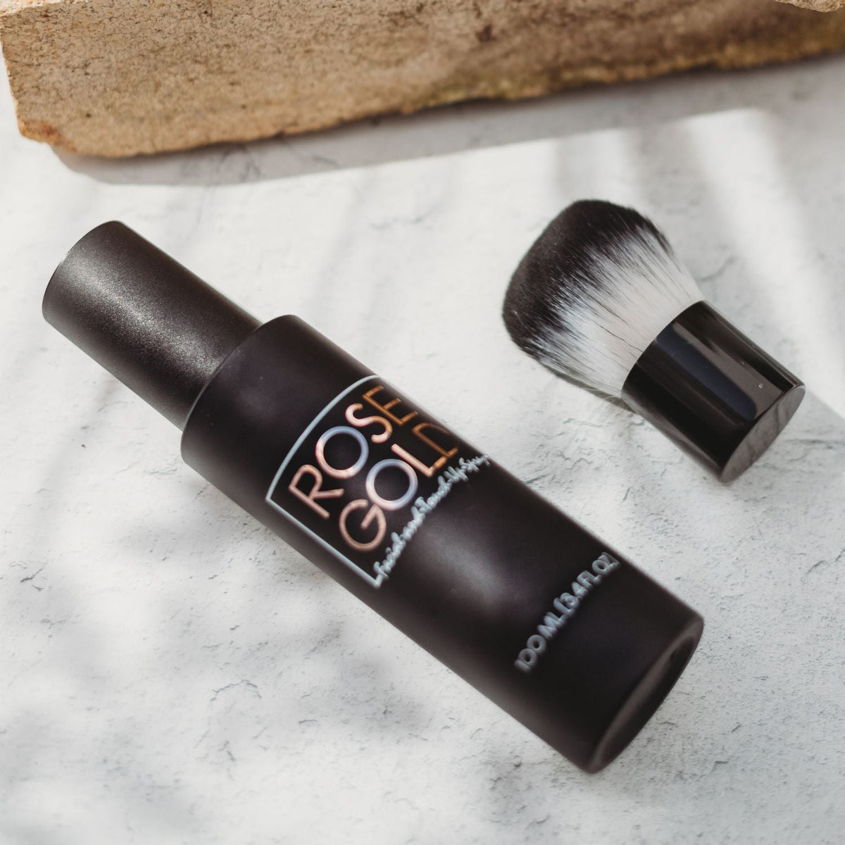 Rose Gold facial tanning mist bottle with angled view, matte black label; makeup brush nearby