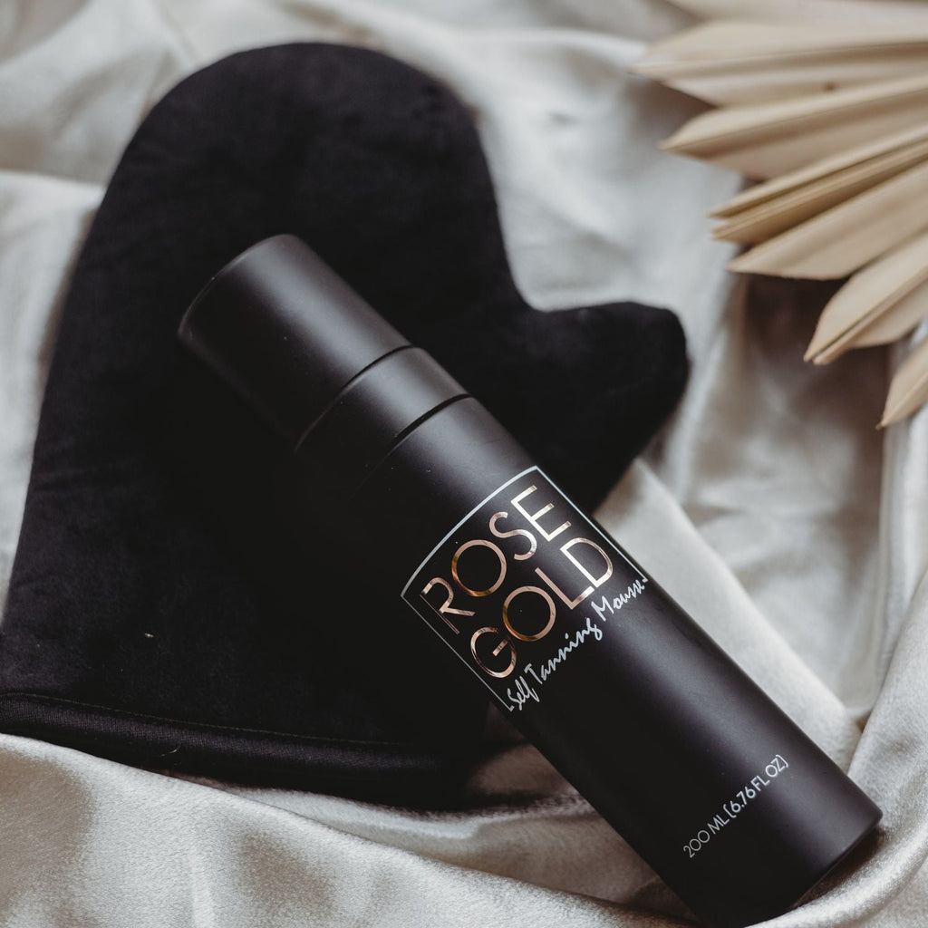 Self-tanning spray bottle with black applicator mitt on light fabric, angled view