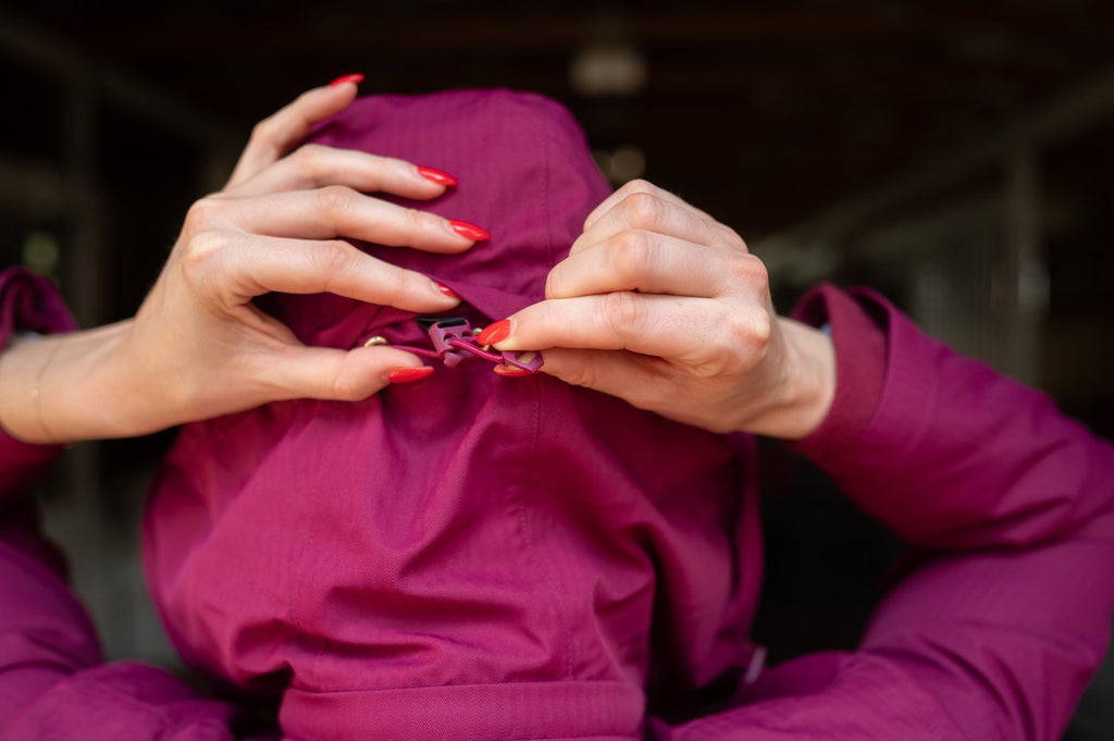 Raspberry insulated jumpsuit chest area with zipper pull as hands adjust it