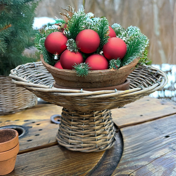 Round woven willow riser basket with red ornaments and pine-like greenery