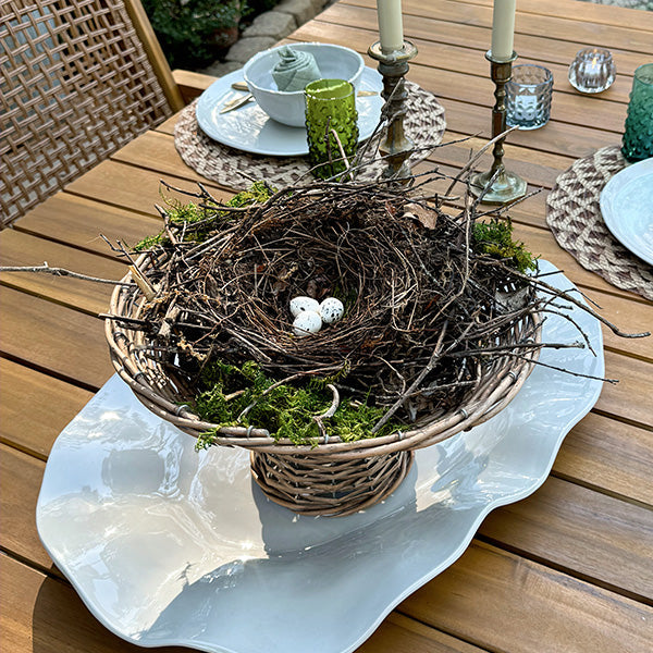 Round woven willow riser basket holding moss and white bird eggs on patio table