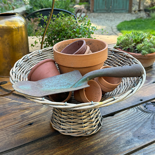 Round woven willow riser basket with terracotta pots and turquoise-gray stones