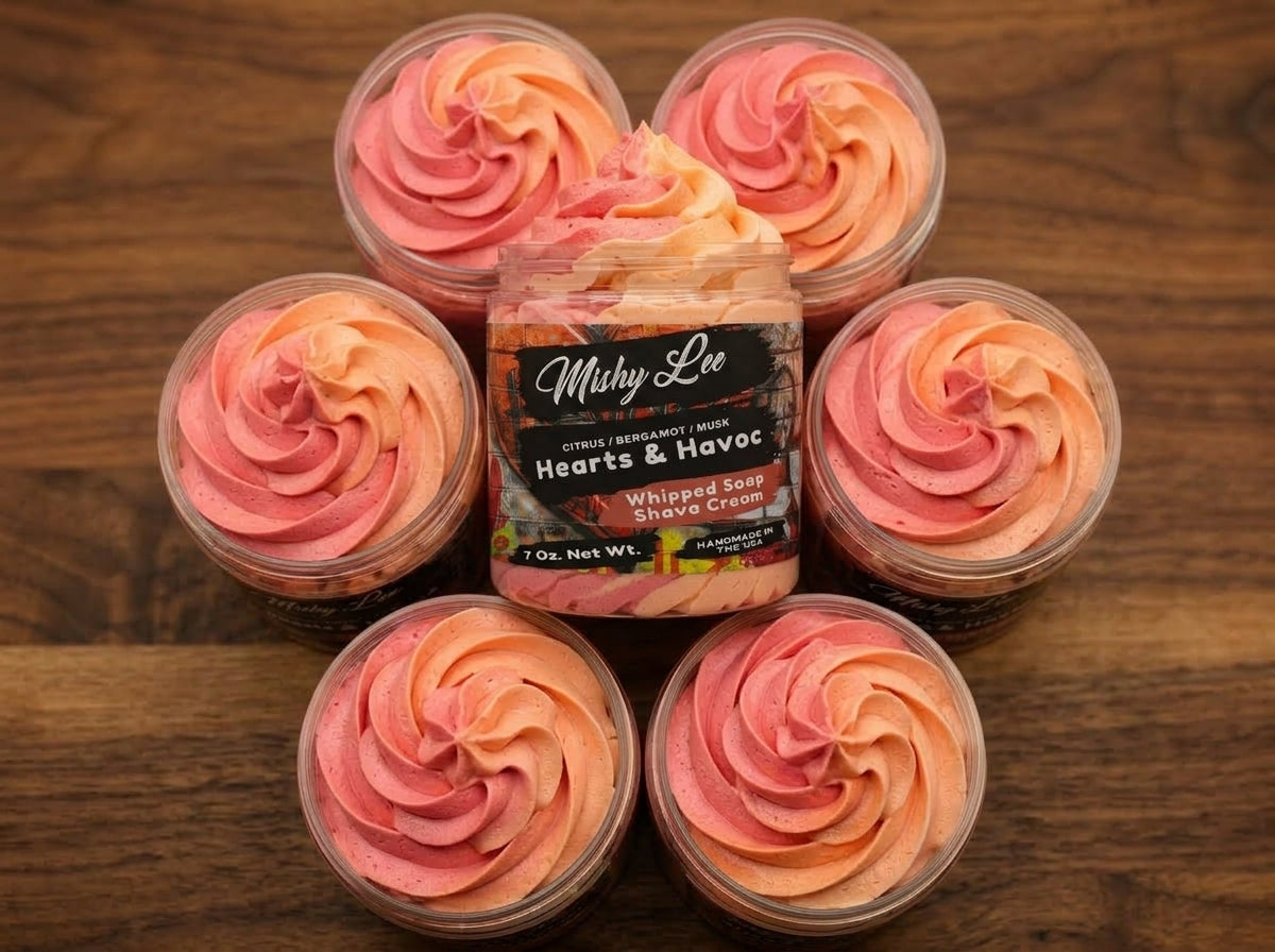 Five small jars of whipped soap with pink-orange swirl tops arranged on wooden surface