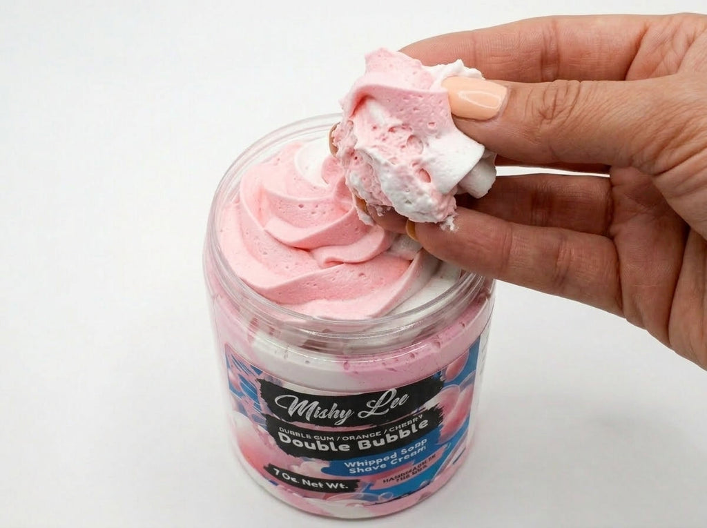 Hand holding a scoop of pink and white whipped soap from the tub