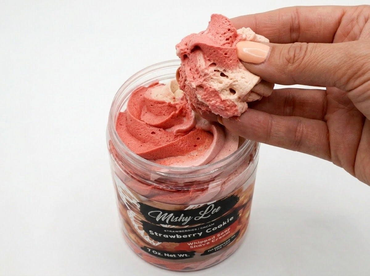 Hand holding pink-and-white whipped soap scoop above open jar