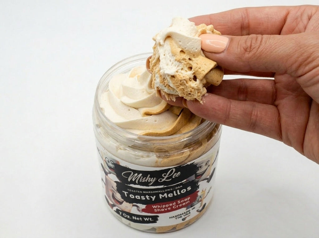 Hand holding a dollop of cream and tan whipped soap from the jar