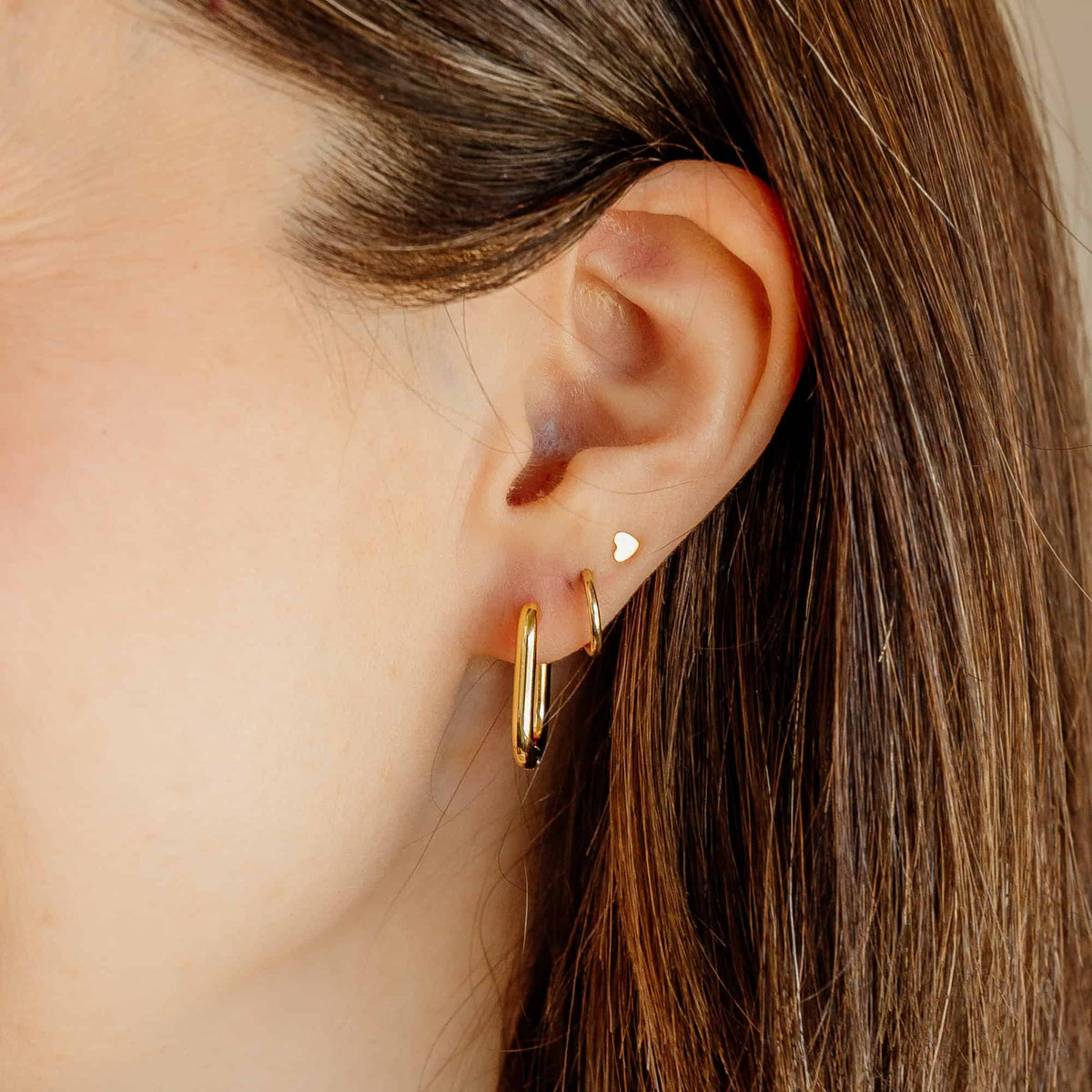 Gold rectangular hoop earrings on ear, small hinged opening visible