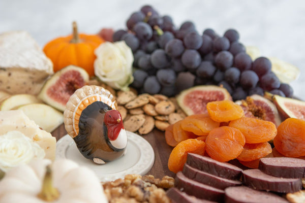 Mini ceramic turkey topper on serving plate, surrounded by fruit and snacks