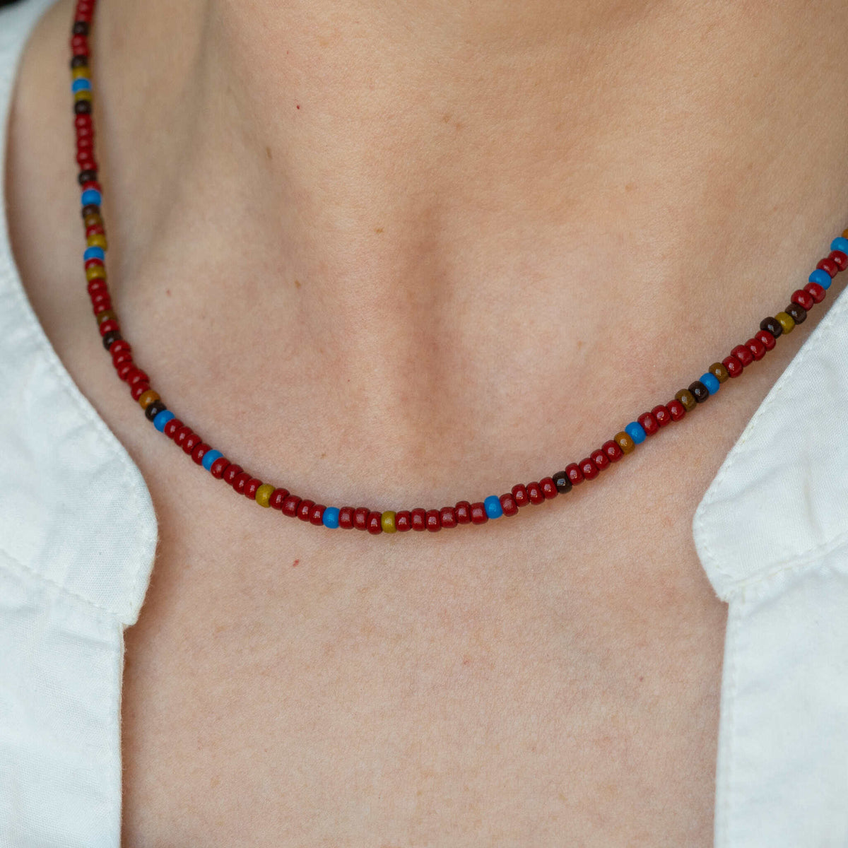 Red beaded necklace with multicolor seed beads, sits at collarbone.