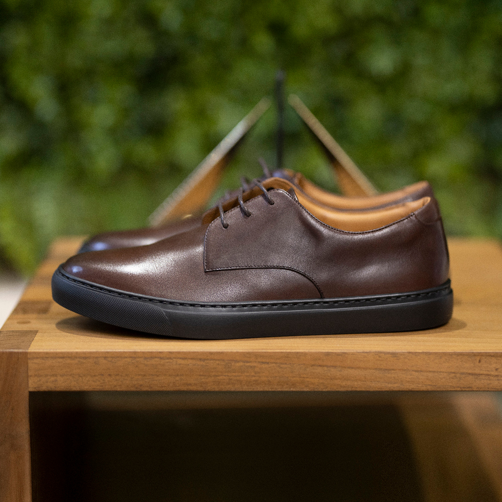 Men's brown leather lace-up oxford shoe on a wooden surface with black rubber sole