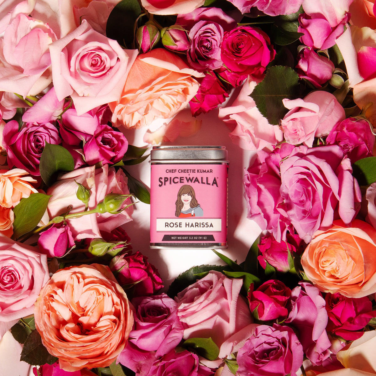 Rose harissa spice tin by Spicewalla with pink label, among pink and orange roses