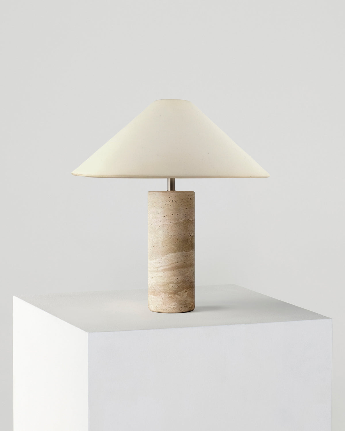 Table lamp with cream fabric shade and beige travertine cylindrical base.