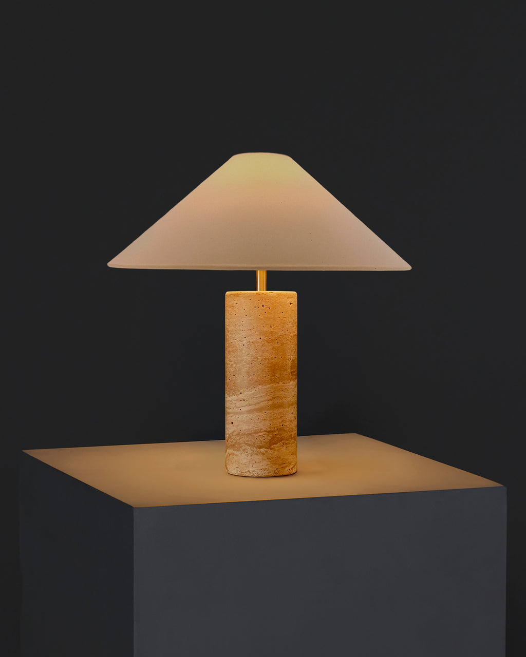 Table lamp with cream fabric shade and textured light tan travertine cylindrical base.