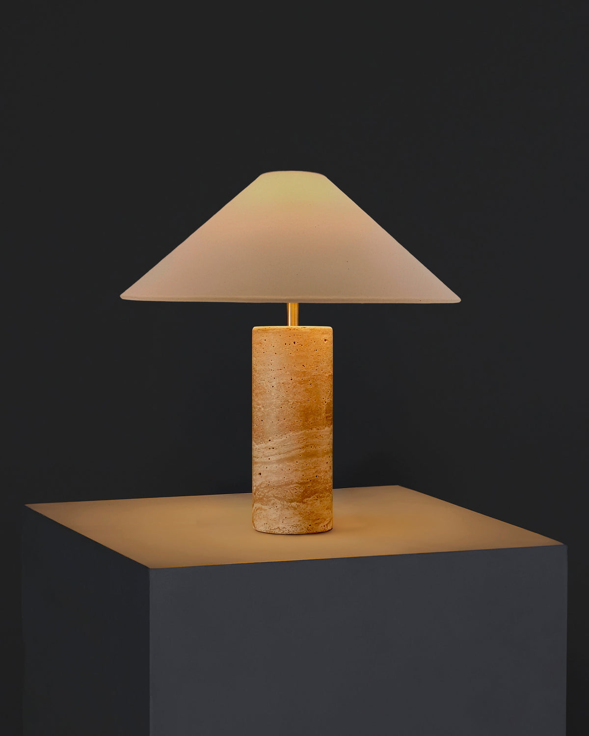 Table lamp with cream fabric shade and textured light tan travertine cylindrical base.
