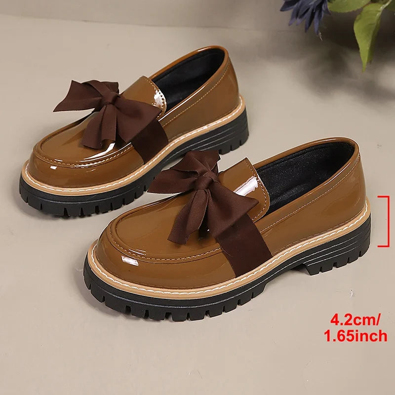 Pair of brown patent slip-on loafers with large bowknot and platform tread sole