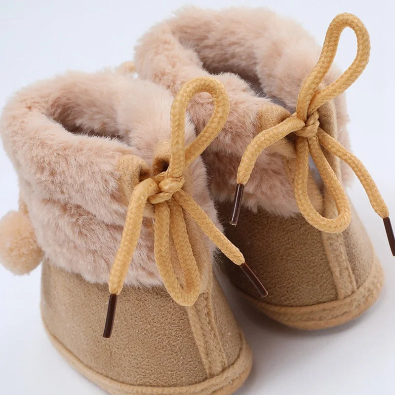 Baby tan booties with plush collar, lace bow ties, and pompom accents; soft sole