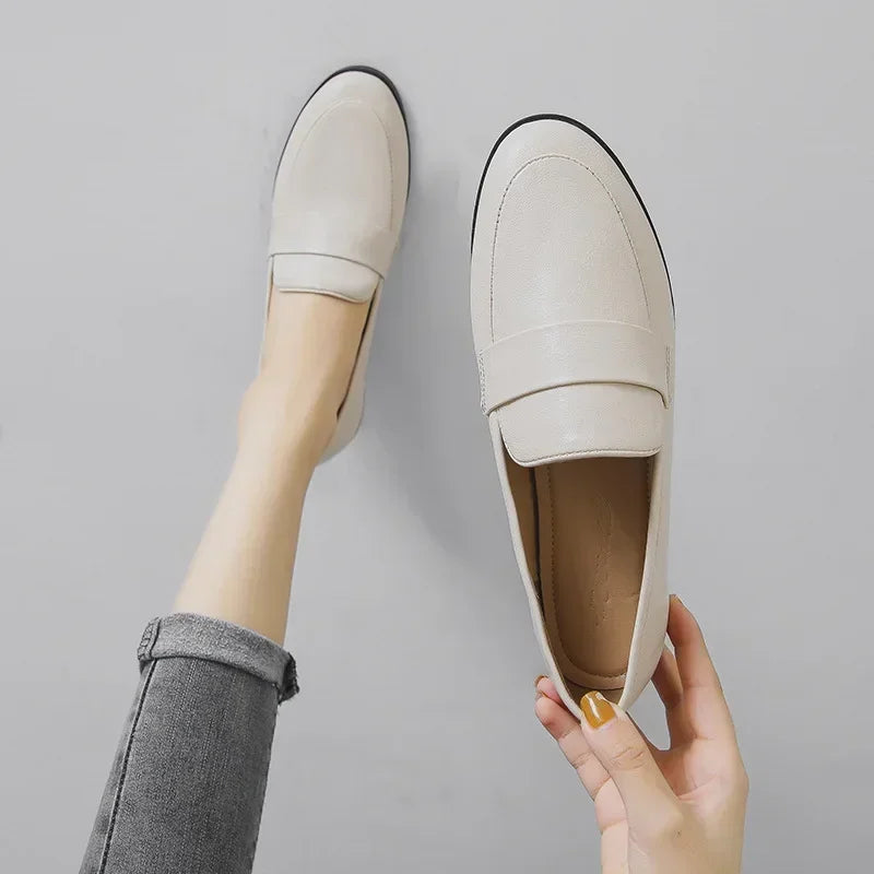White slip-on loafers with rounded toe and strap detail, shown with legs and socks