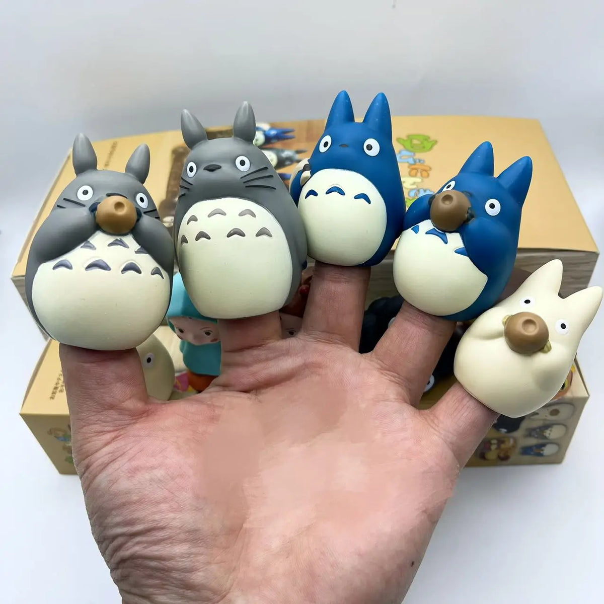 Hand holding a row of cartoon blind box figurines in blue, gray, and cream