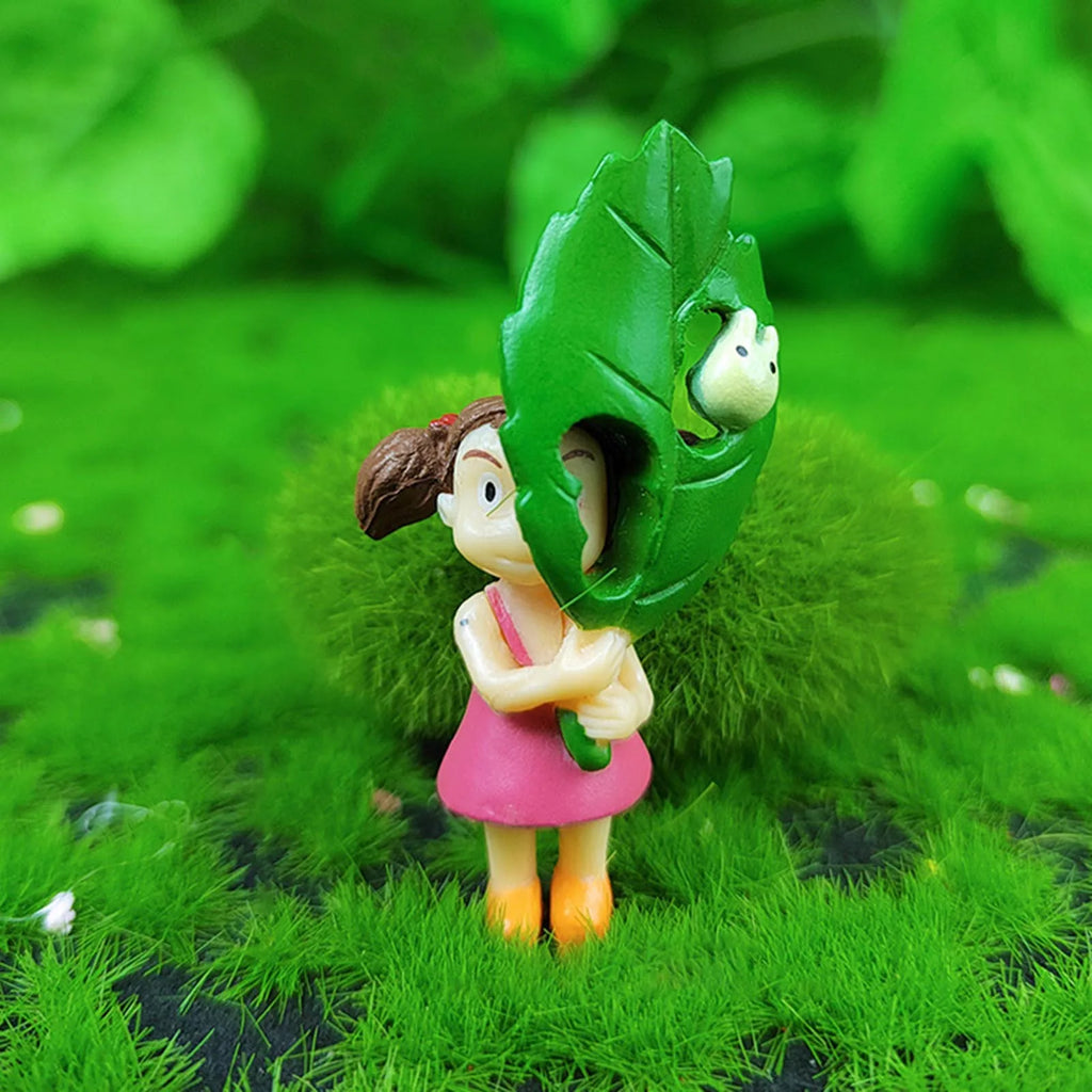 Green leaf animal figurine on grass, holding a small child in pink dress