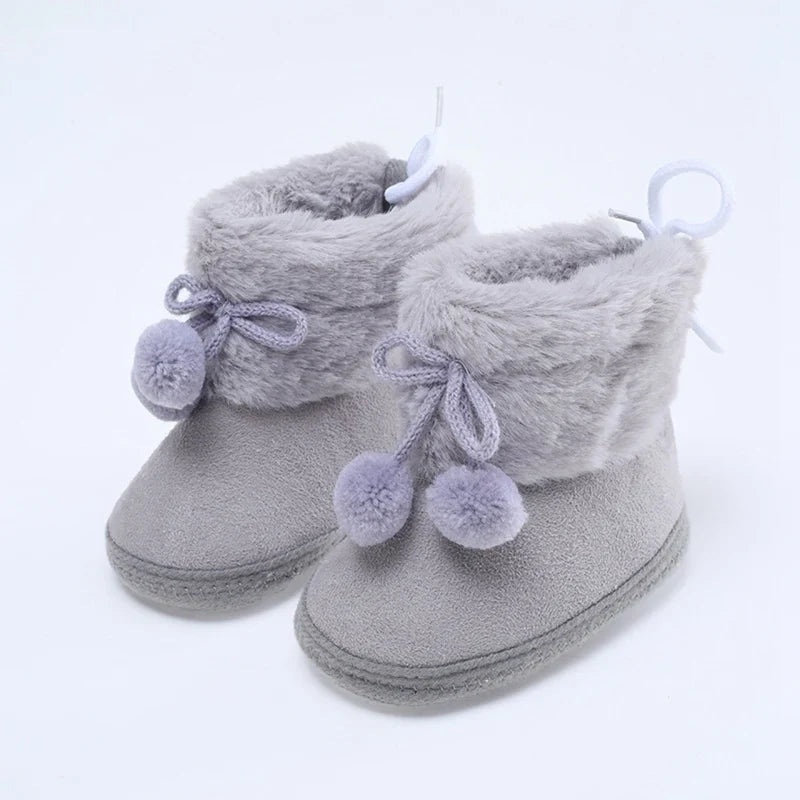 Baby light gray booties with plush lining, lace bow ties, and pompom accents; soft sole