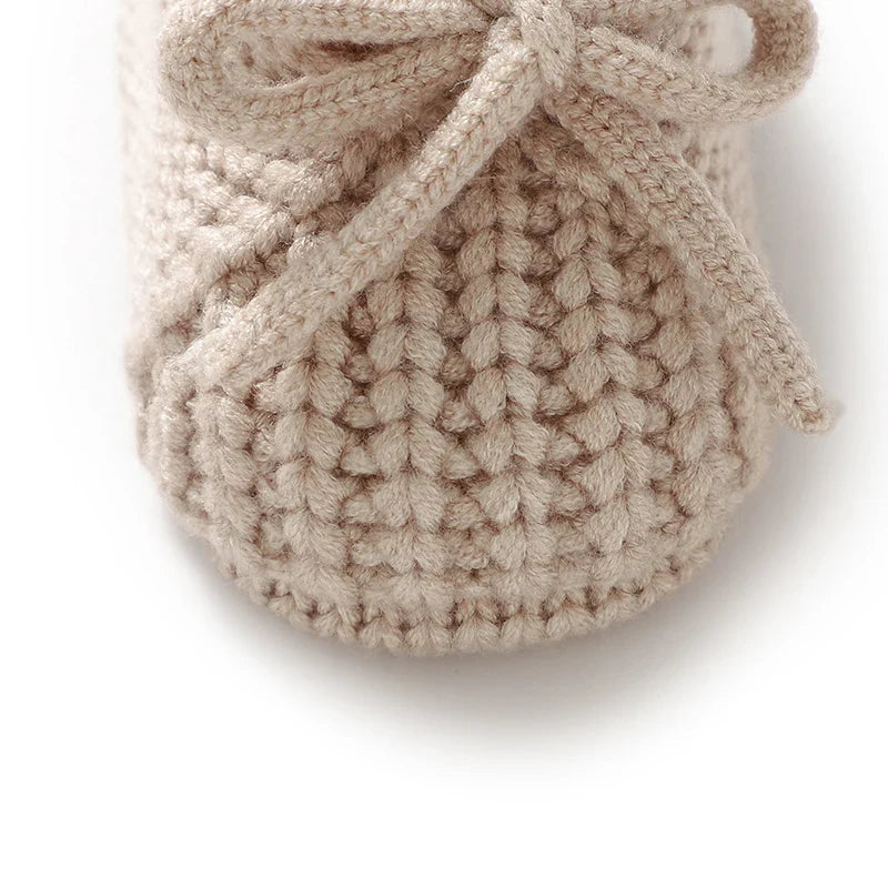 Beige knitted baby bootie with textured knit and tie lace bow