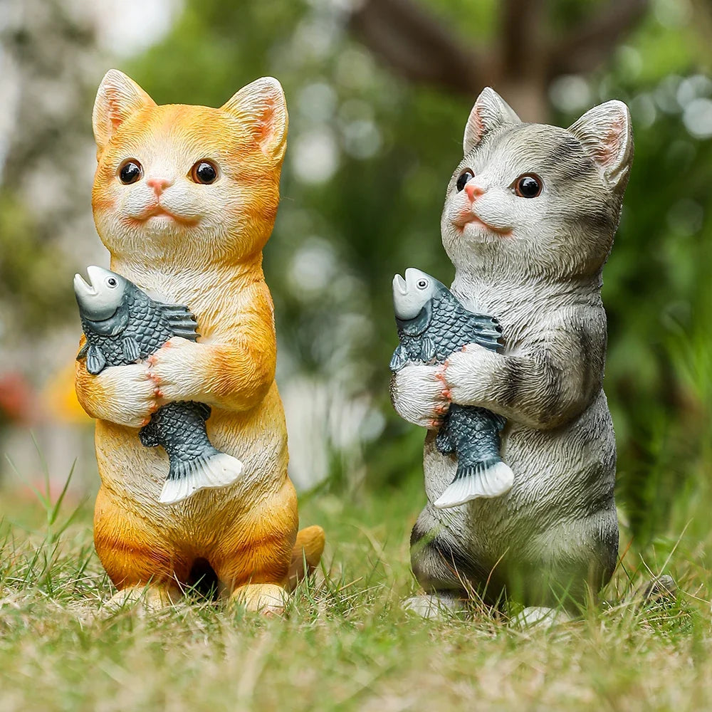 Orange cat figurine sitting on grass, holding a gray fish in its paws