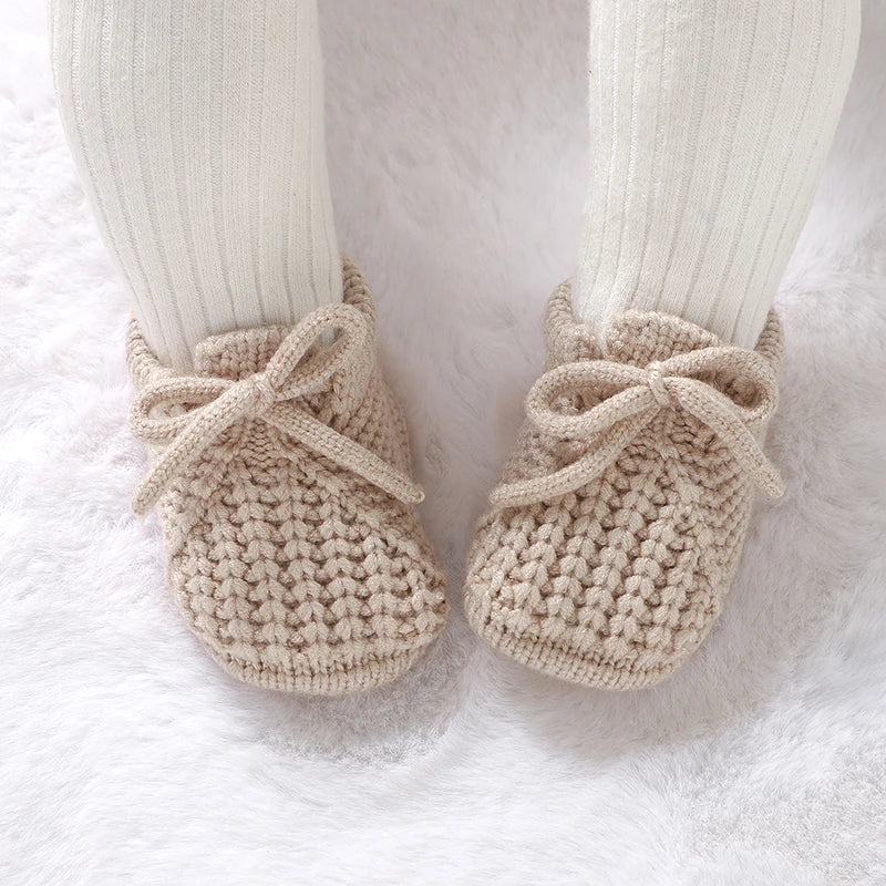 Beige knitted newborn booties with bow tie laces, worn with matching socks