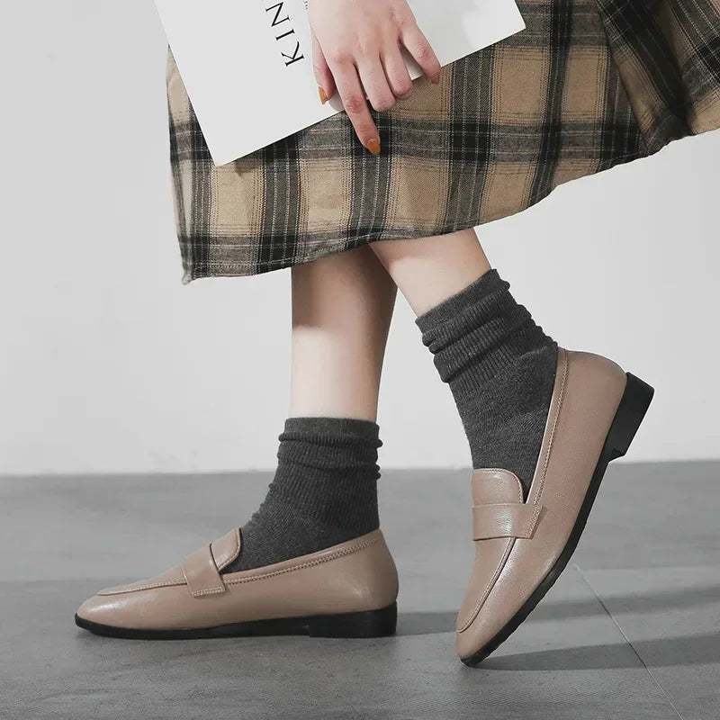 Beige slip-on loafers with round toe worn with black socks and a plaid skirt