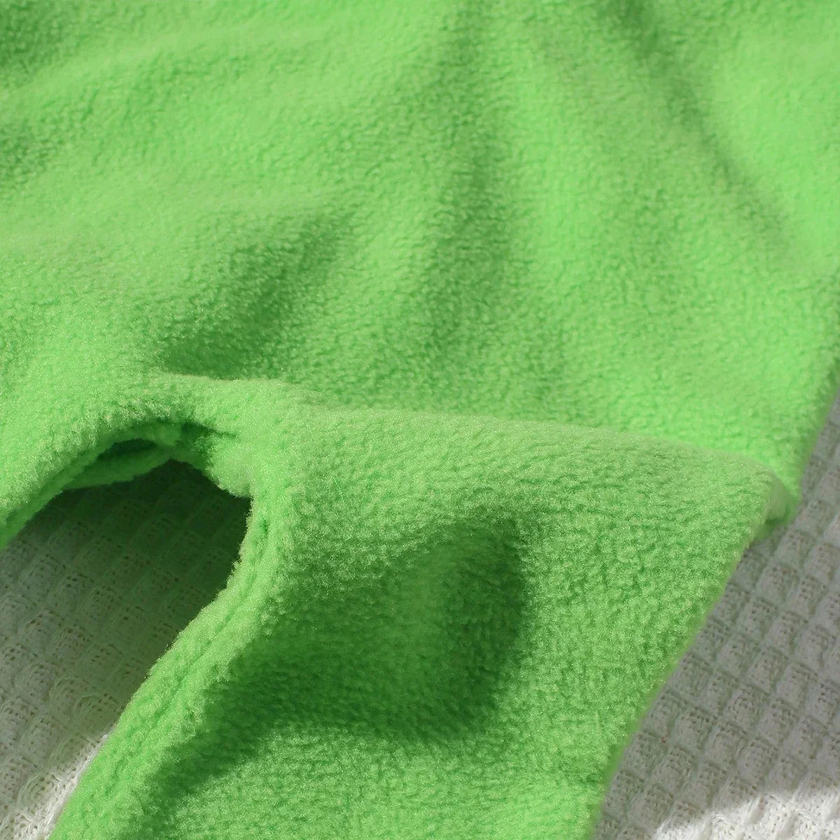 Green plush dinosaur jumpsuit fabric close-up with soft textured weave