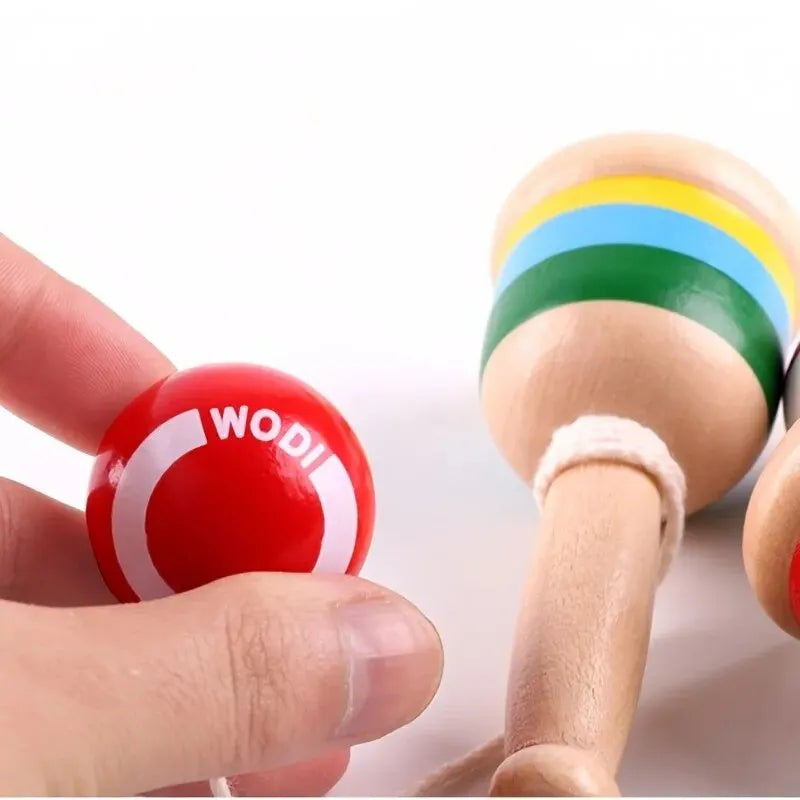 Hand holding a wooden cup-and-ball handle with a red ball on a string
