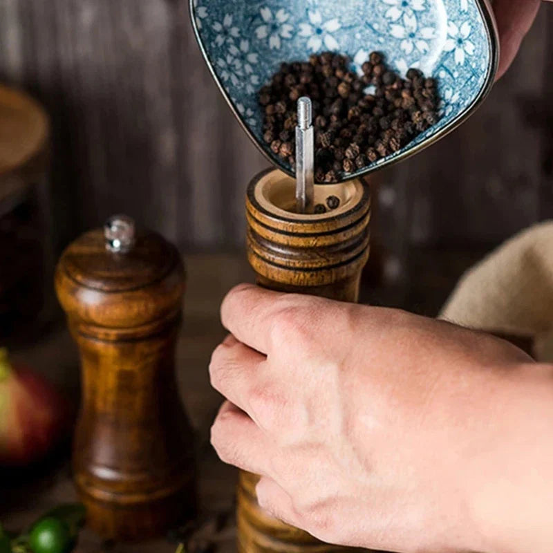 Handheld oak wood pepper mill grinding black pepper into a bowl