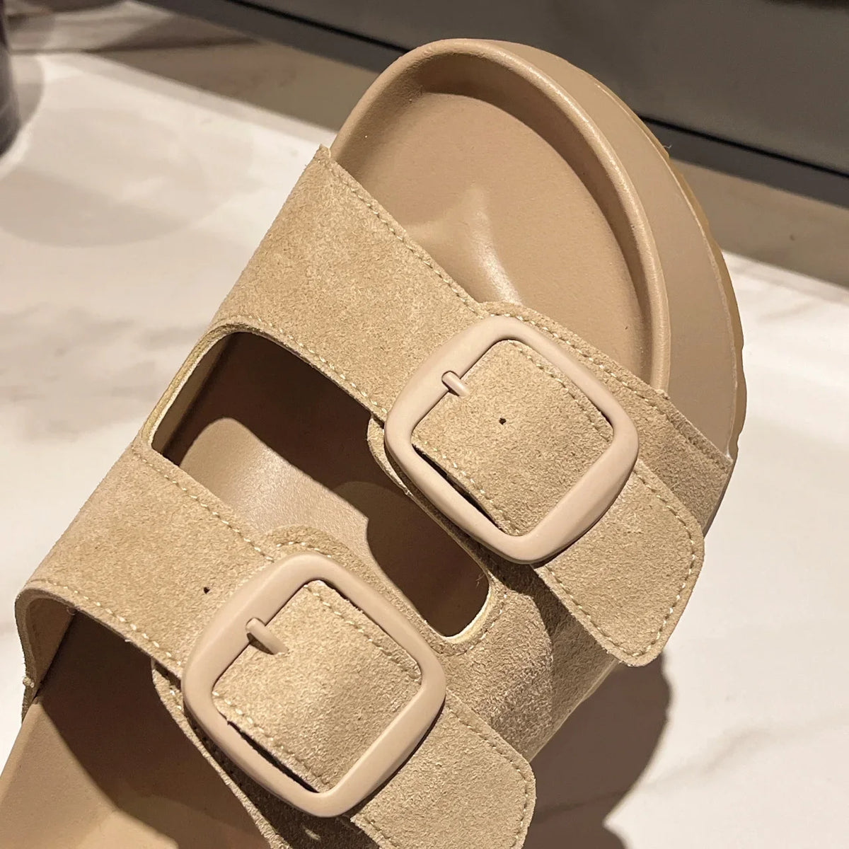 Beige suede-look platform slide sandals with two square buckle straps.