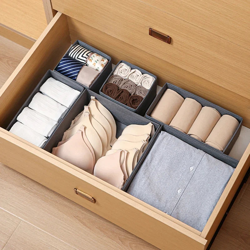 Gray foldable fabric storage bins arranged in a wooden drawer for clothing essentials