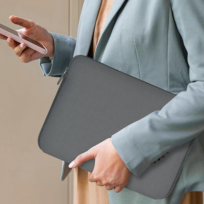 Grey laptop sleeve carried in a hand, zippered protective laptop case.