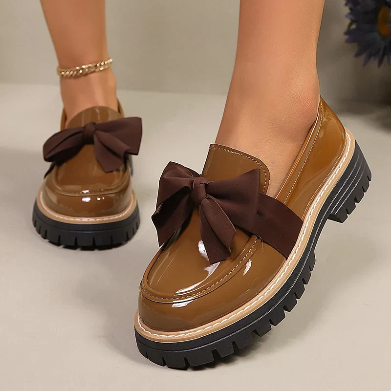Brown patent loafers for women with dark bow; chunky platform lug sole, slip-on style.