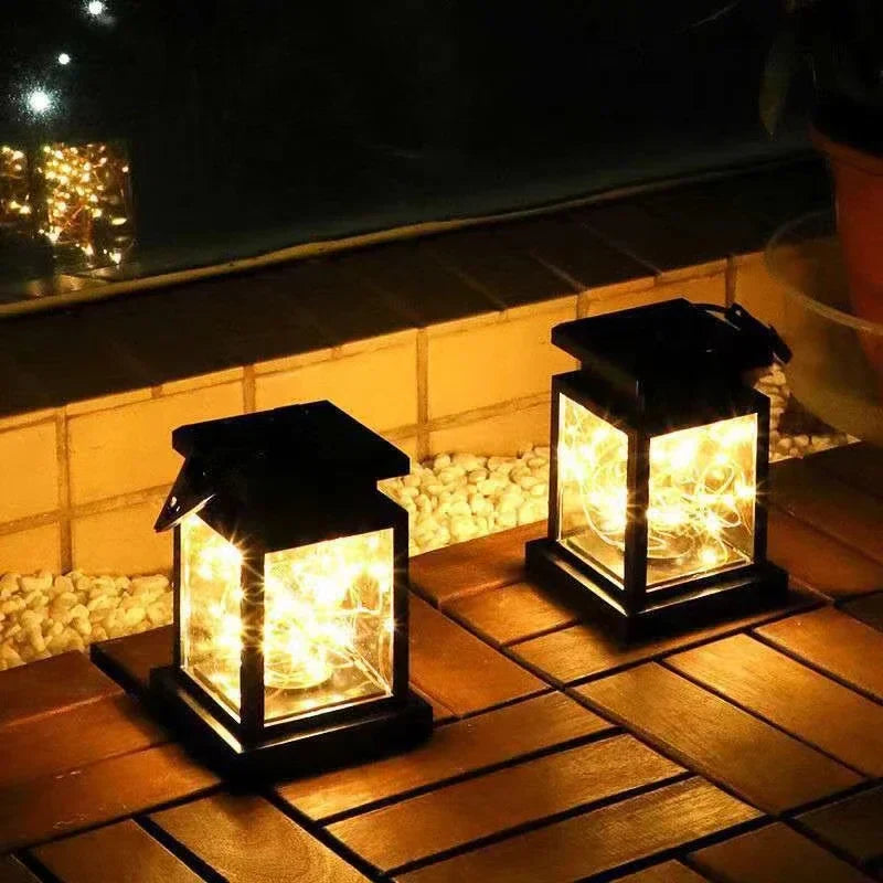 Black solar lantern on tiled patio step, glowing warm light inside clear glass