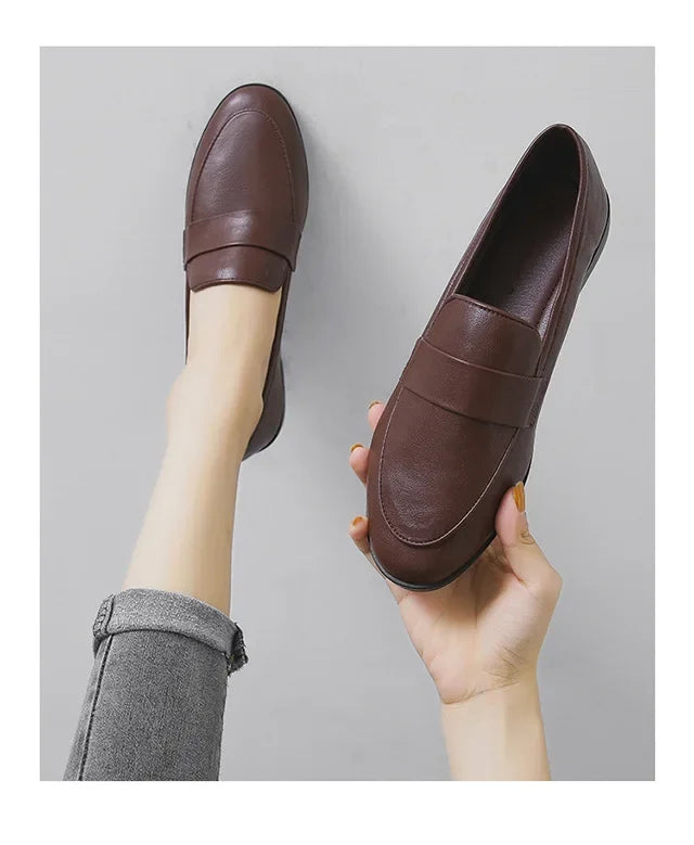 Brown slip-on loafers with rounded toe, one shoe held up for a side view
