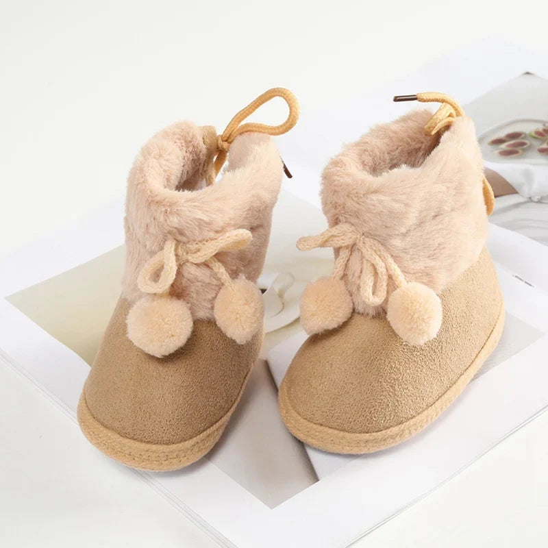 Baby suede-style booties with fuzzy lining, bow laces, and pompom trim; tan