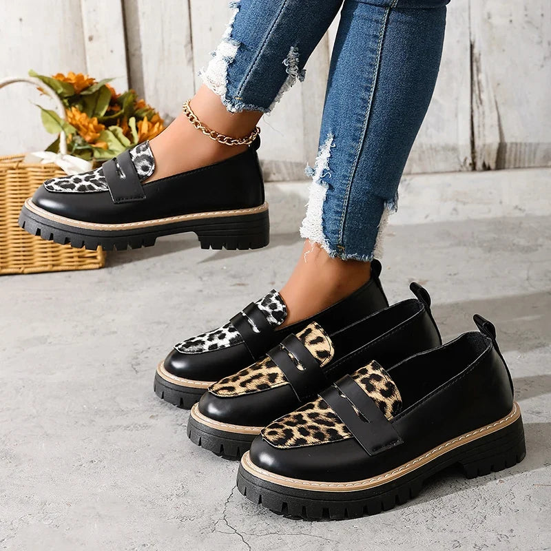 Pair of black platform loafers with leopard print panels and buckle straps.