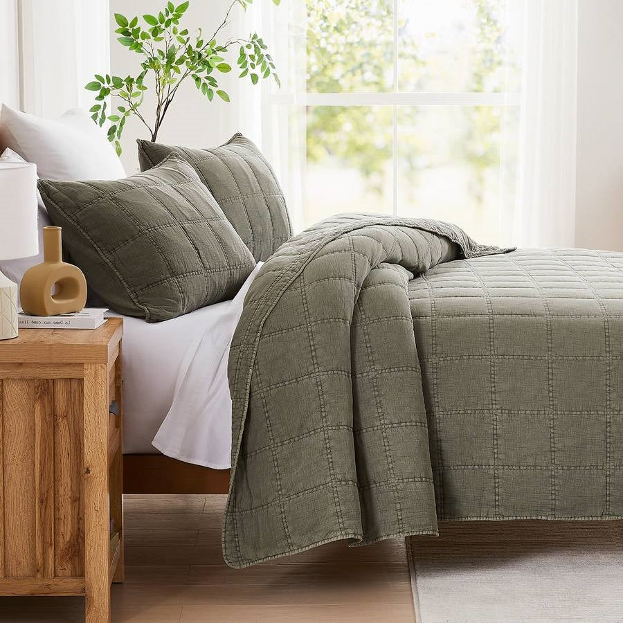 Sage green cotton quilt set with two shams and draped corner on bed