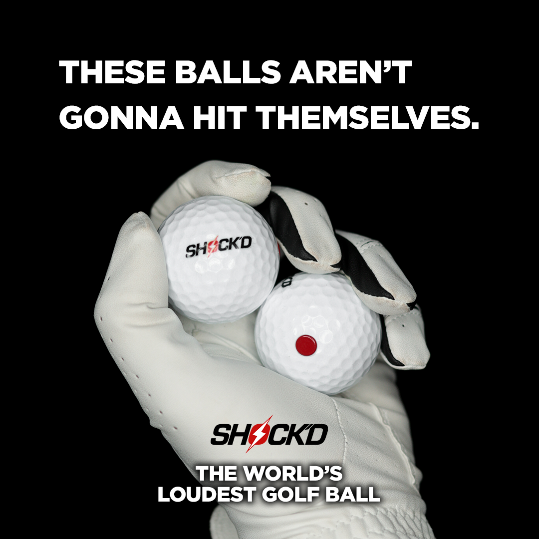 Gloved hands holding two SHOCK'D golf balls, one with a red dot center.