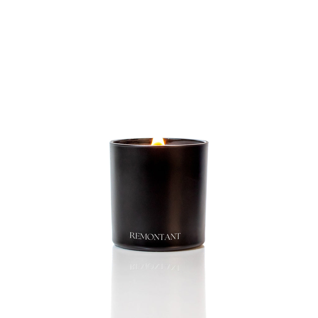 Black glass wood wick candle with centered lit flame and Remontant label